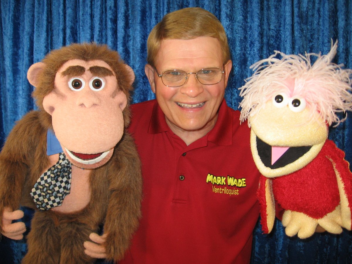 Mark Wade in a red polo with a monkey figure and a pink-haired bird figure